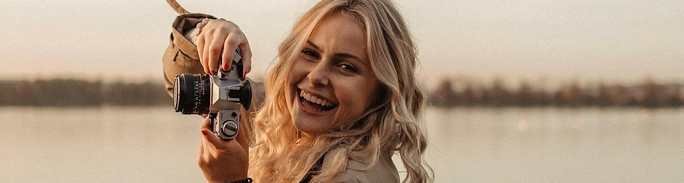 lachende blonde junge Frau mit einer analogen Kamera neben dem Gesicht