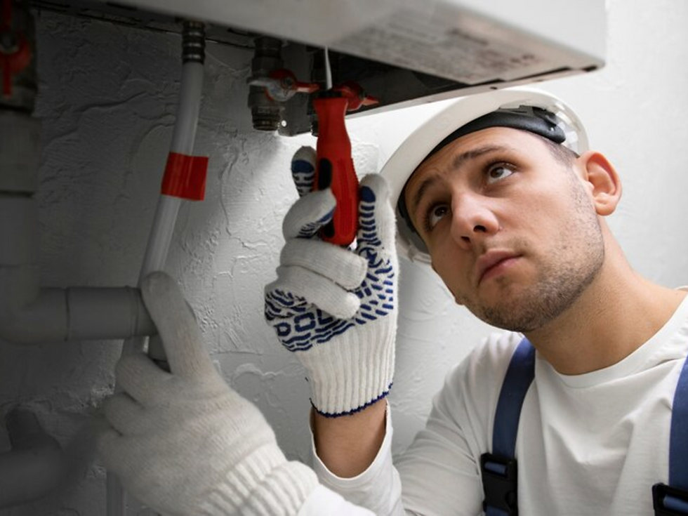 Worker in white helmet and gloves using a wrench on pipes. Gray background with focused expression, red tool adds contrast.