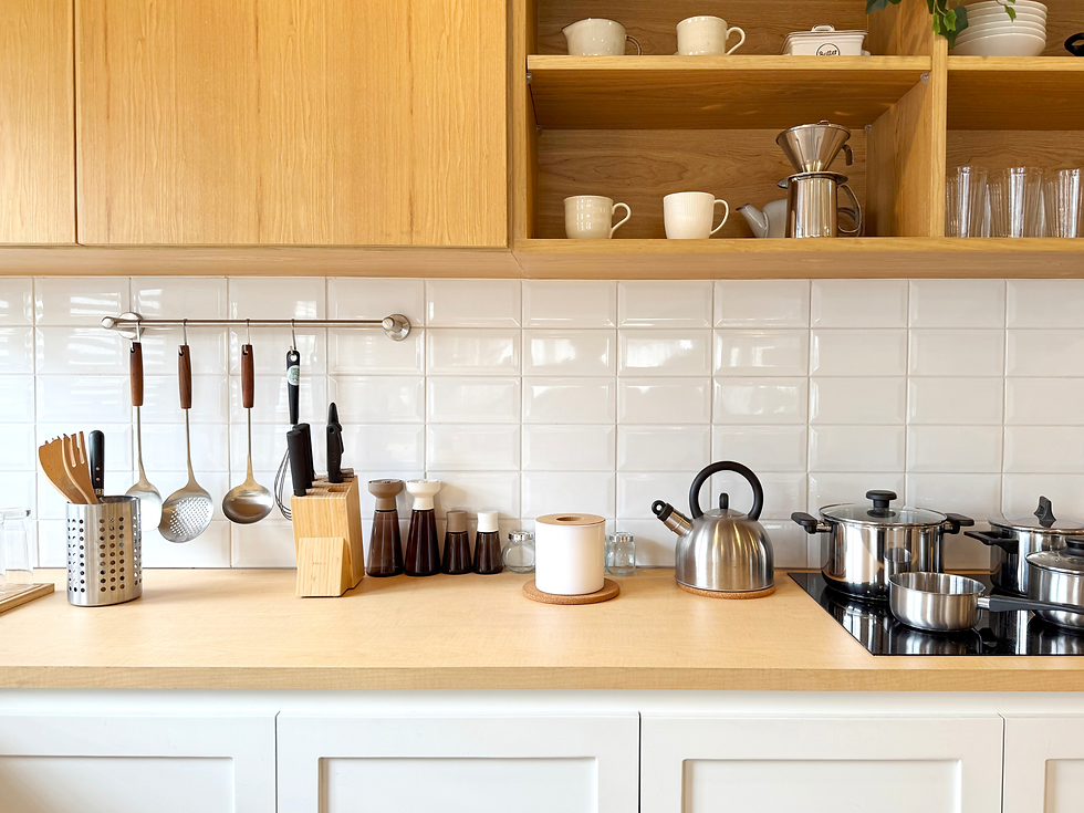 Modern kitchen countertop with utensils, knives, and pots. White tiles, wooden shelves with cups, kettles, and spices create a tidy look.