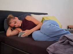 Jugendliche liegt deprimiert auf dem Bett und schaut ins Handy.