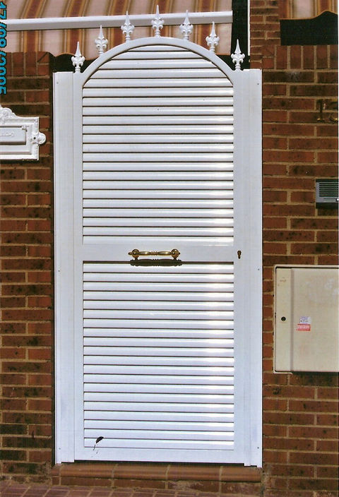 Puerta de entrada peatonal con un suave arco y panel macizo inferior.