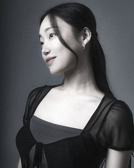 Portrait of Sol, a smiling tattoo artist with short hair, glasses, and a tropical-patterned shirt, photographed in black and