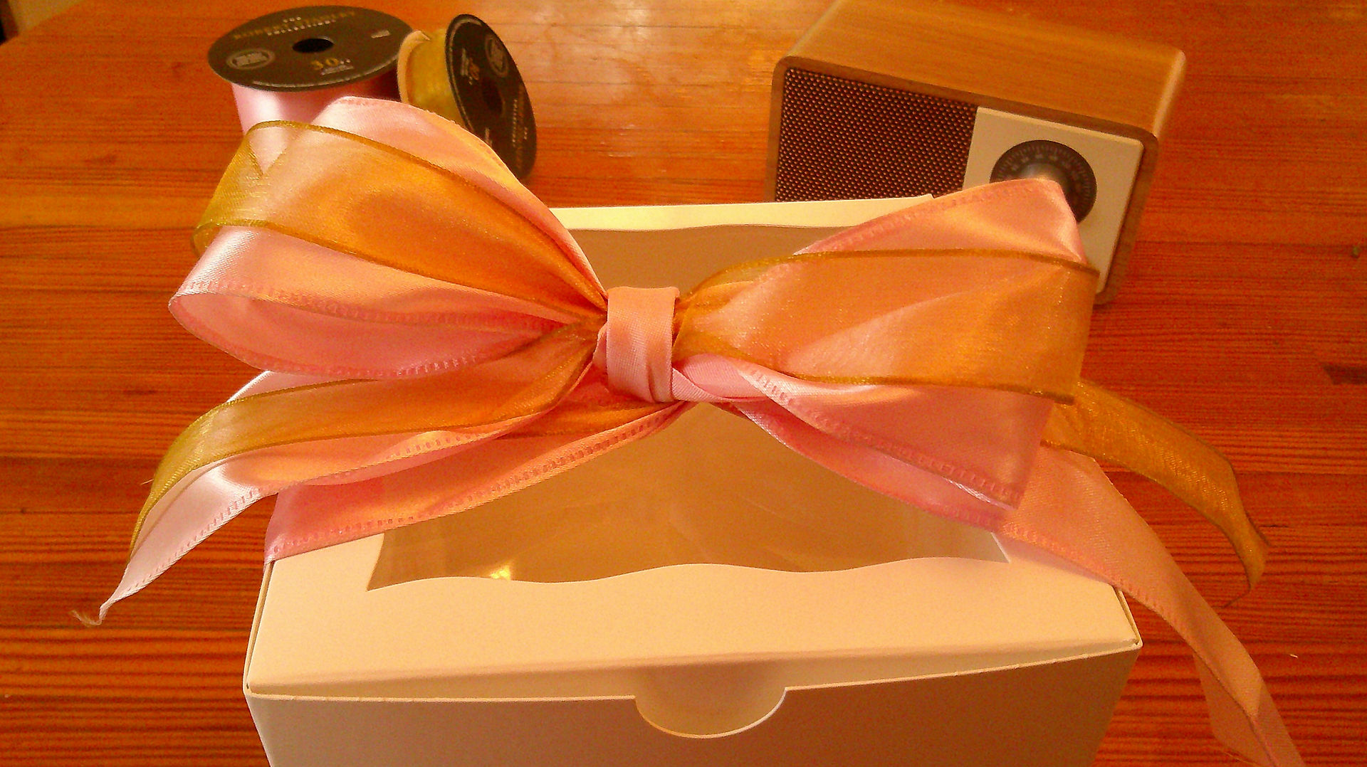 A white box with pink and gold ribbon in a bow.