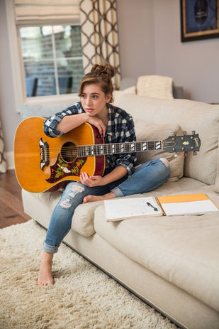 Linde holding her Gibson guitar, sitting on the couch