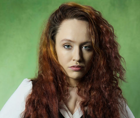 Professional corporate portrait of a red-haired woman on a green background.
