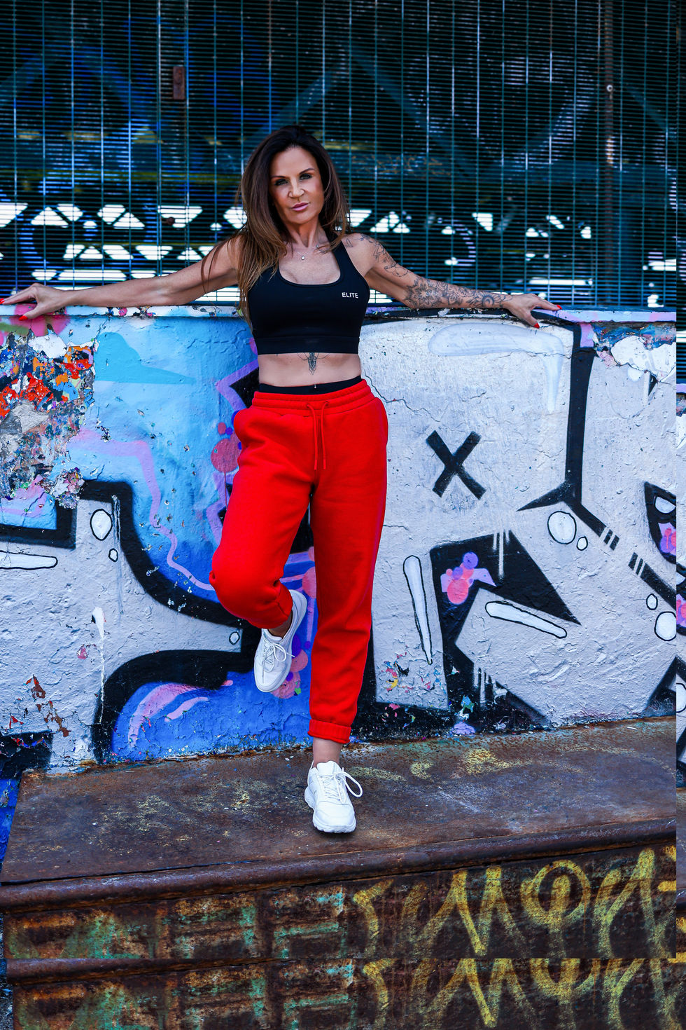 Woman in red tracksuit pants and a black training top standing on a ramp at a skatepark - urban fashion photoshoot in colour.