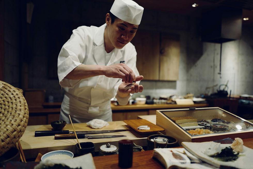 Japanese chef in white uniform and hat carefully plates sushi at a dimly lit restaurant counter.