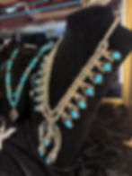 Ornate silver squash blossom necklace with turquoise stones on black display.