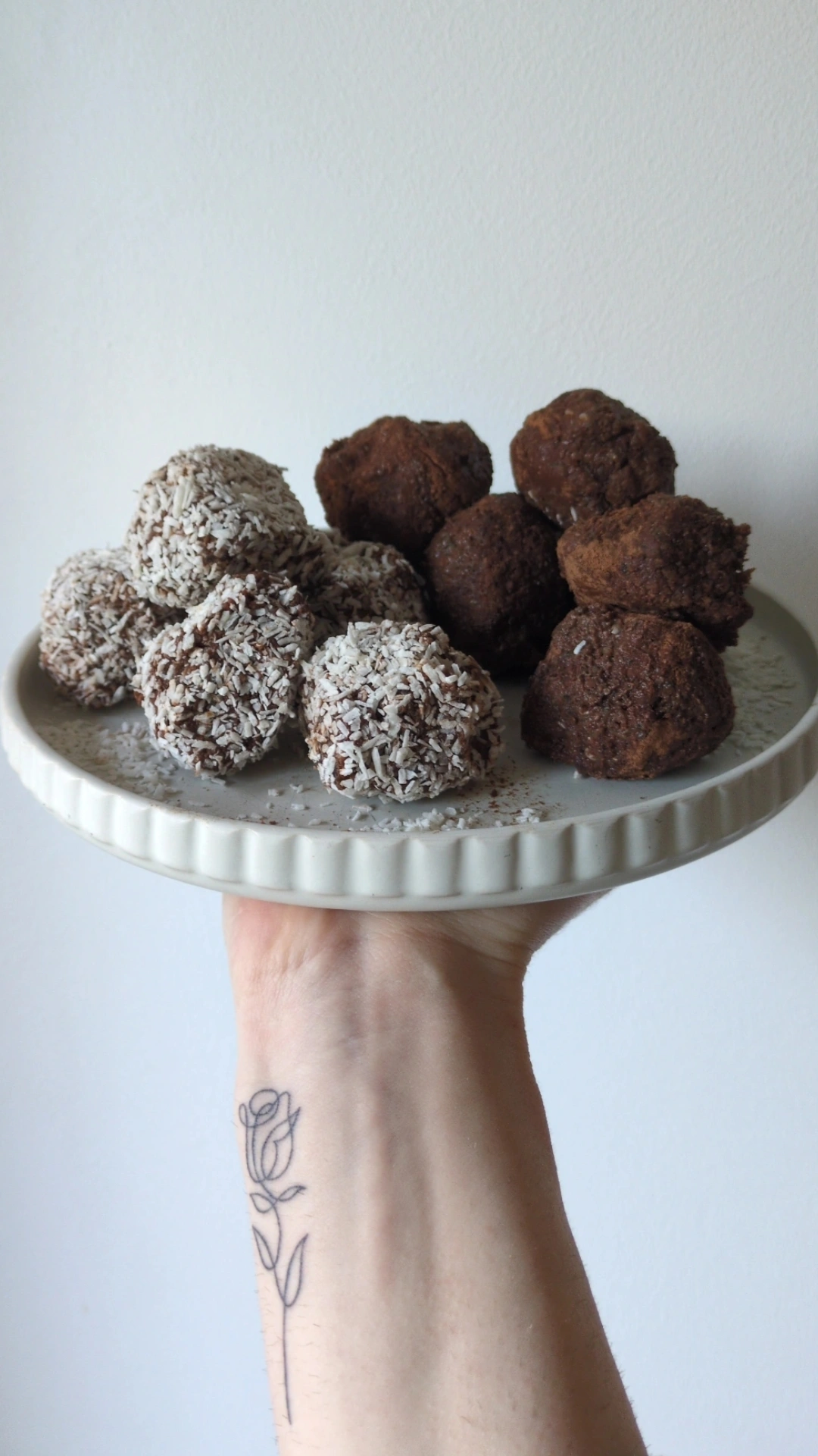Hand- held plate of hojicha chcolate date bliss balls coated in coconut and cacao, a hormone-supportive snack rich in healthy fats and fibre.