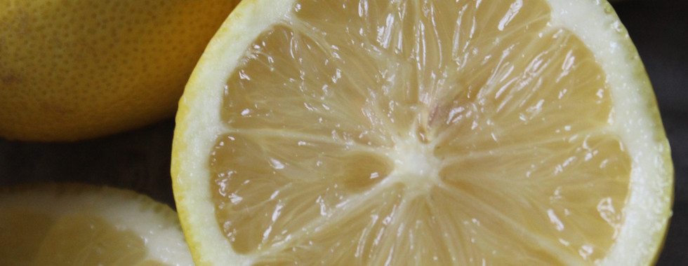 Fresh lemons, one sliced in half on a grey surface- used in Balanced Imogen's matcha pesto linguine recipe to support liver detoxification of hormones and iron absorption from plant-based ingredients. 