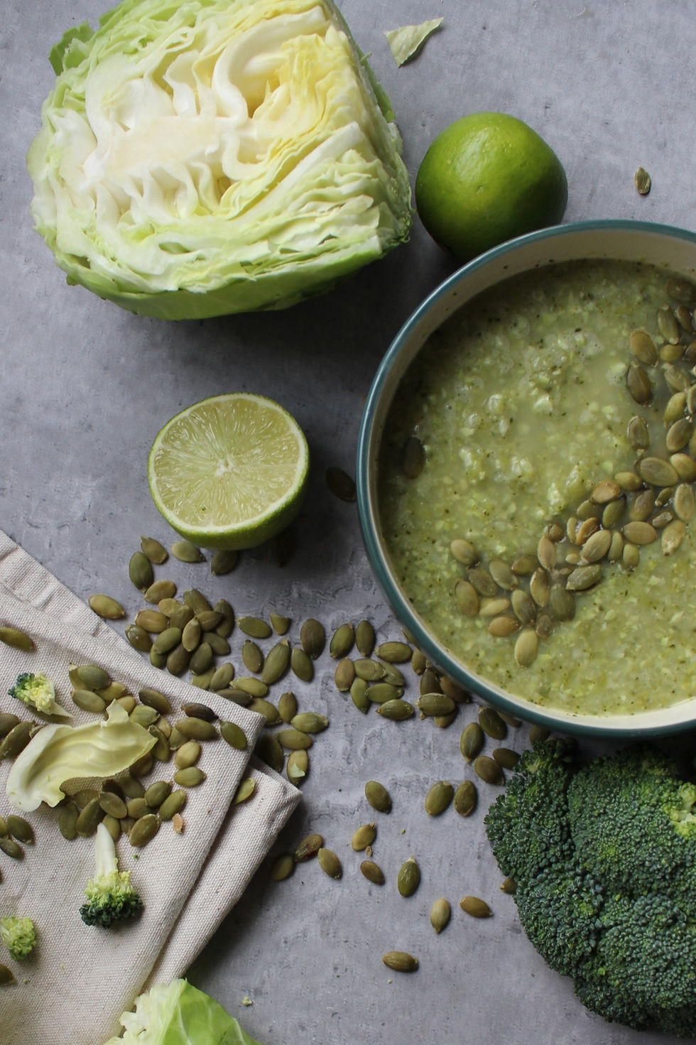 Hormone balancing Green Soup styled on concrete surface with broccoli, cabbage, lime and pumpkin seeds highlighting food-first hormone support.