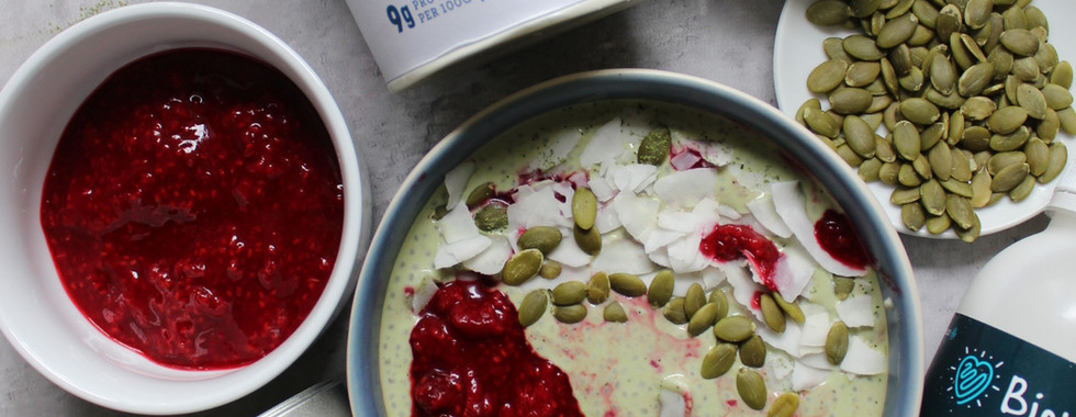 Overhead flat lay of Balanced Imogen's creamy matcha and raspberry chia pudding- styled with Yeo valley Greek yoghurt, Biomel coconut kefir, grade AA Organic OMG Matcha Tea, pumpkin seeds, coconut shavings and homemade raspberry compote, a cycle-synced breakfast for the follicular and ovulatory phases.