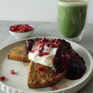 Matcha latte beside French toast topped with berry compote, Greek yoghurt and pomegranate seeds