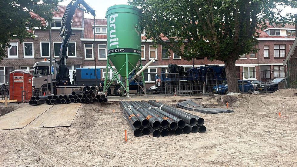 Bouwterrein in woonwijk met stapels zwarte buizen, hijskraanwagen en groene Bruil-silo tussen bomen en rijtjeshuizen.