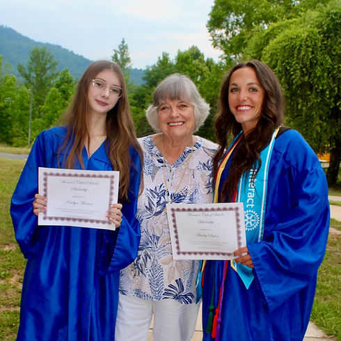 Two Womens Club of Saluda scholarship recipients in blue robes holding awards with the President of the Womens Club..