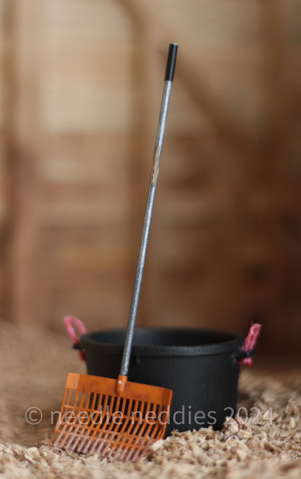 Thumbnail: An orange shavings fork with a silver handle, leaning against a black muck bucket with pink handles.