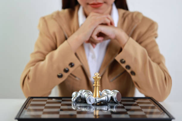 Businesswoman hands in classic suite sitting and clasping hands planning strategy with chess on white table.
