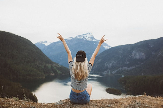 Woman sitting on cliff raising both hands.