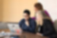 Three women beside table looking at laptop