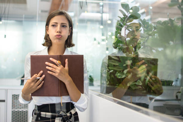 Portrait of beautiful young business woman pouting and holding notebook in office.
