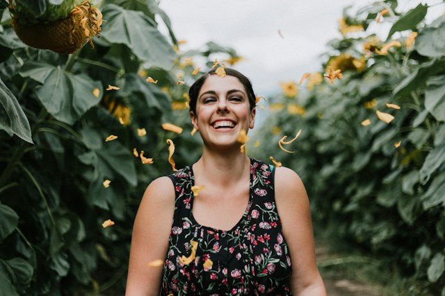 Happy woman in floral top standing in the middle of sunflowers