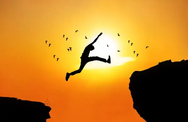 Silhouette of man jumping a wide cliff. Shot outdoor at sunrise