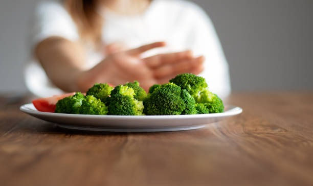 girl pushing away plate with broccoli and other vegetables refusing to eat