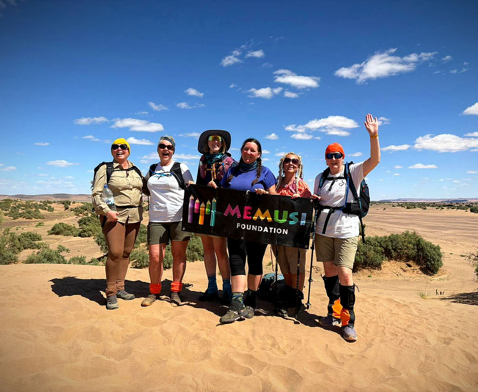 A group of Memusi Foundation volunteers celebrating the completion of a Sahara desert trek, holding a charity banner to mark