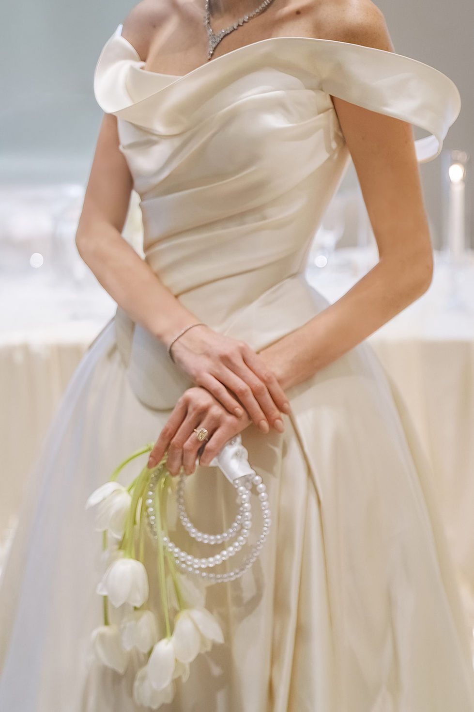 Detail of an ivory satin wedding gown with a bouquet of white tulips and pearls