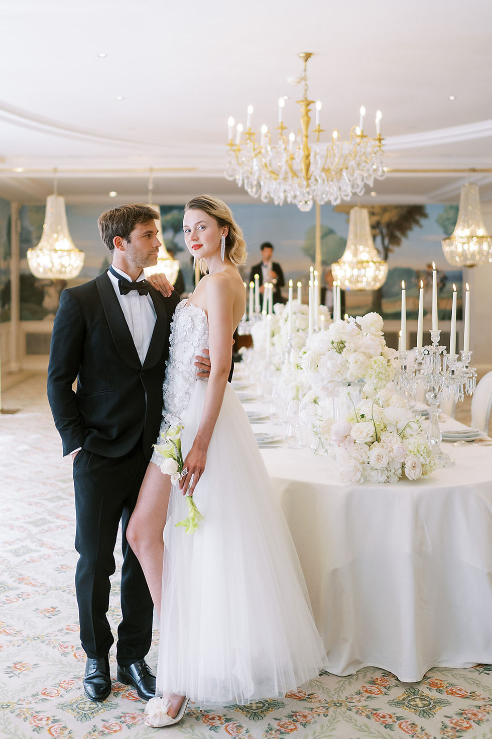 Mariés élégants devant la table dressée sous les lustres en cristal, bouquet de callas et roses blanches, fleuriste mariage Bristol Paris