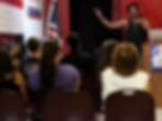 A man speaking at a podium to an audience near a US flag.