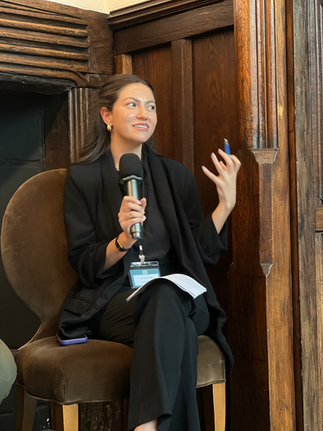 A panelist speaking into a microphone while seated, looking upward and gesturing during the panel discussion at Foundation House.
