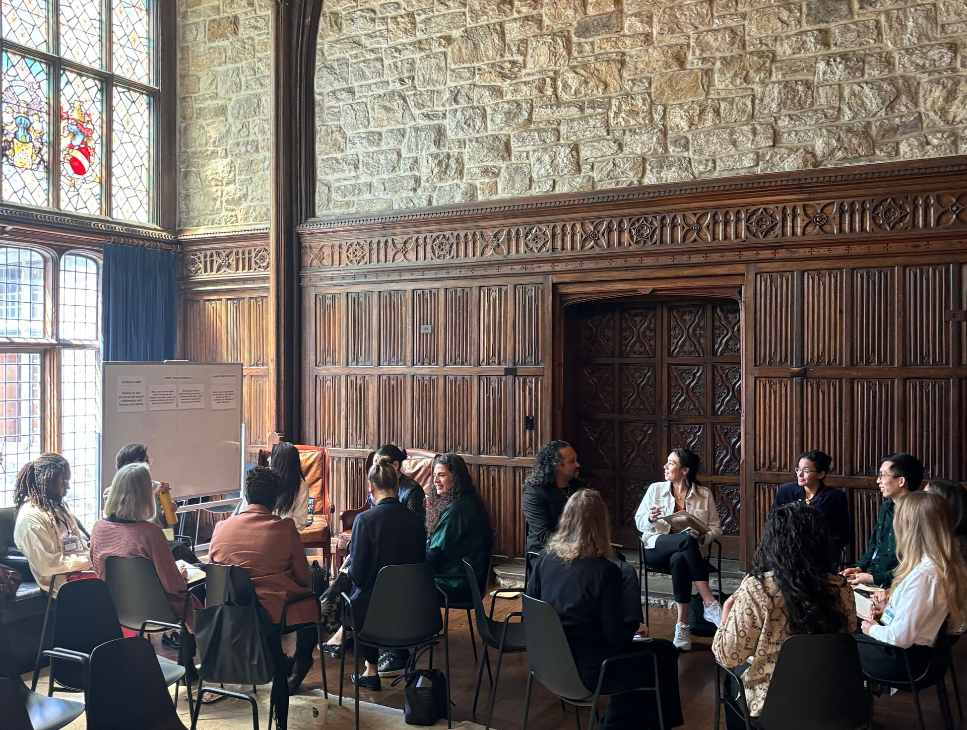 Attendees gathered in a circle in an elegant room with ornate wooden paneling, stained glass windows, and decorative stone walls, engaged in discussion during a breakout session at Foundation House.