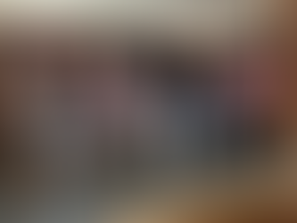 Four THE REAL Ambassadors wearing THE REAL branded caps sit in chairs on a raised platform in front of a ornate fireplace, each holding a microphone. The man on the left speaks animatedly while gesturing with his hand during the panel discussion.