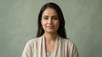 Portrait of a woman with long dark hair and a beige top, looking at the camera against a soft green background, calm expression