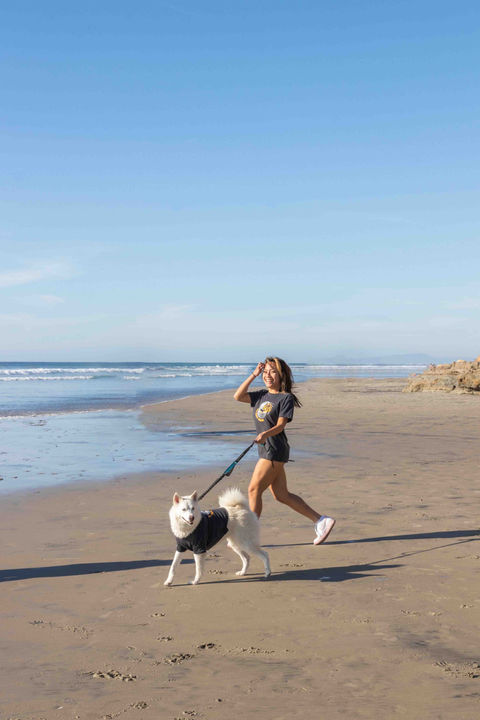A woman walking her pup on dog beach wearing matching dog and people t-shirts