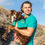 Thumbnail: A man with his dog in shirts with Tails on Trails designs with a dog hiking and trees and mountains in background