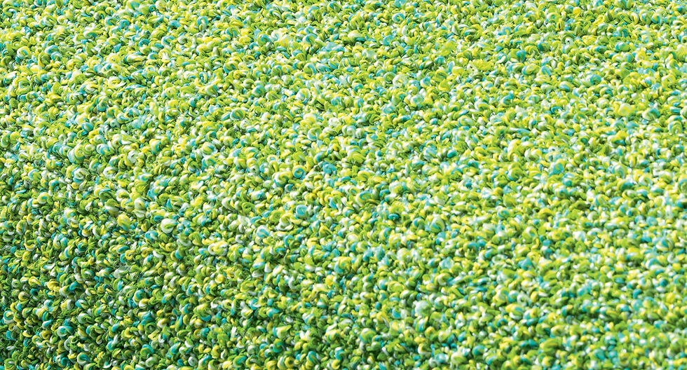 Close-up of a textured surface with green and yellow looped fibers, creating a vibrant, plush appearance. No text or figures present.
