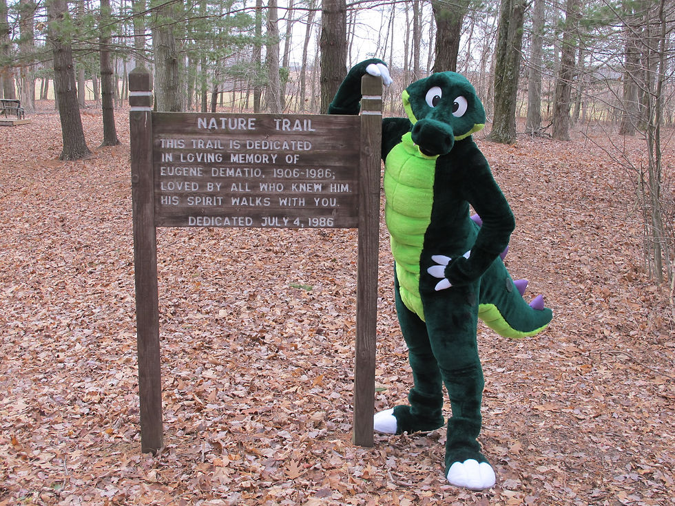 A gator mascot next to a sign in the woods