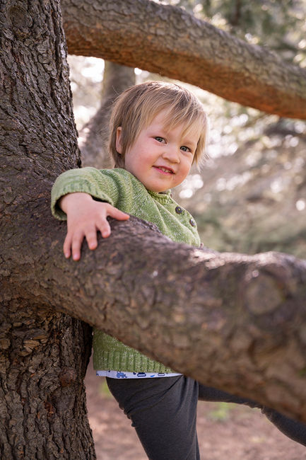 Toddler son leaning on a tree, smiling at the camera - lifestyle shot. Greenwich Park, London.