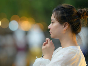 Woman in a white blouse looking thoughtfully into the distance against a softly blurred outdoor background.