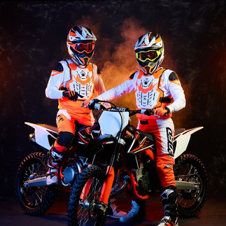 18-jähriger Fox-Pilot kniet im Kies, zieht seinem Kumpel die dreckigen Motocross-Stiefel aus, intensive Nähe unter Männern