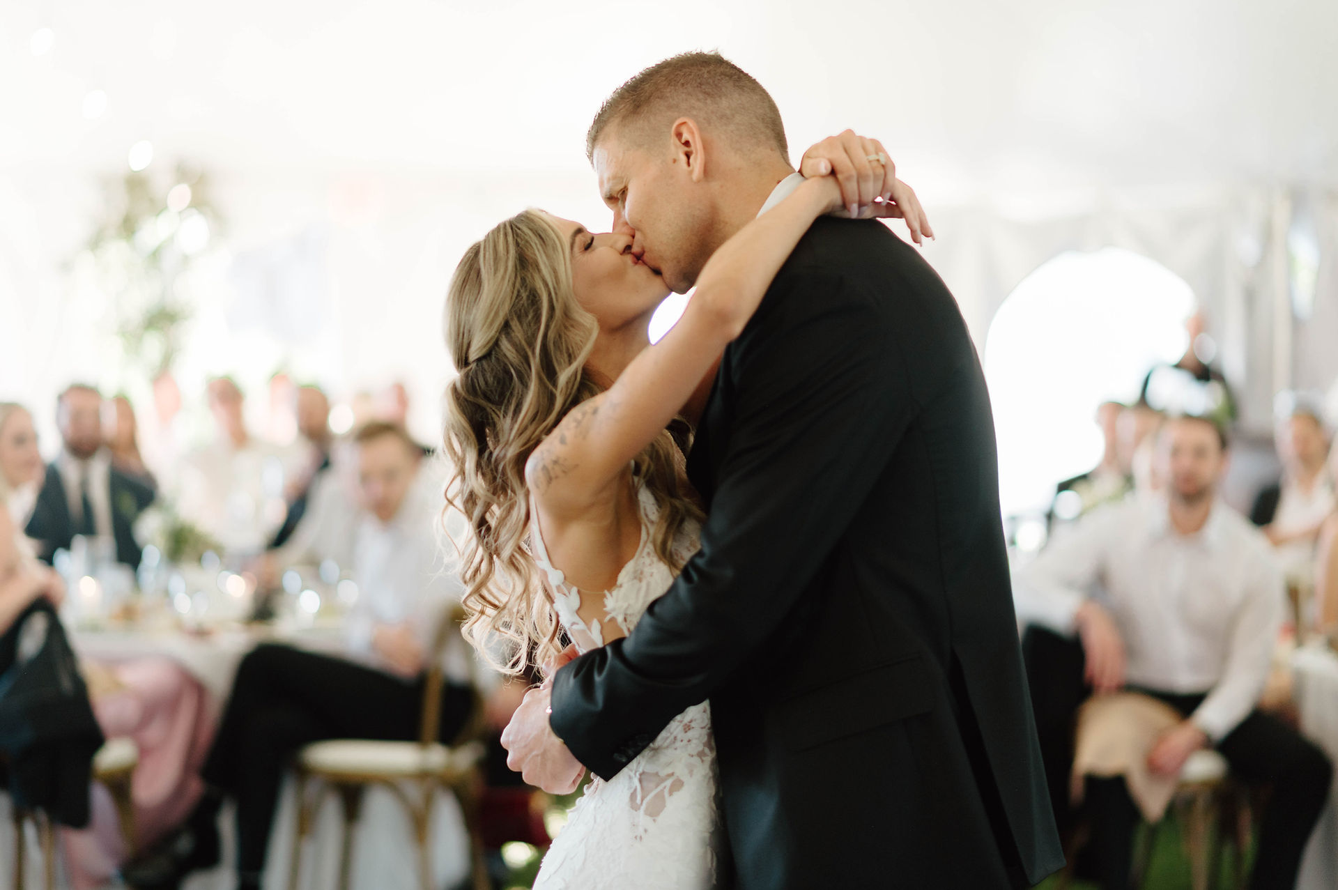 Bride and groom kissing as they share the first dance together surrounded by friends and family members