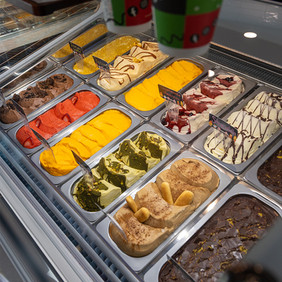 Gelatos de múltiples sabores alineados en vitrina refrigerada.