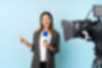 reporter-woman-holding-microphone-reporting-news-blue-wall-pointing-finger-side.jpg