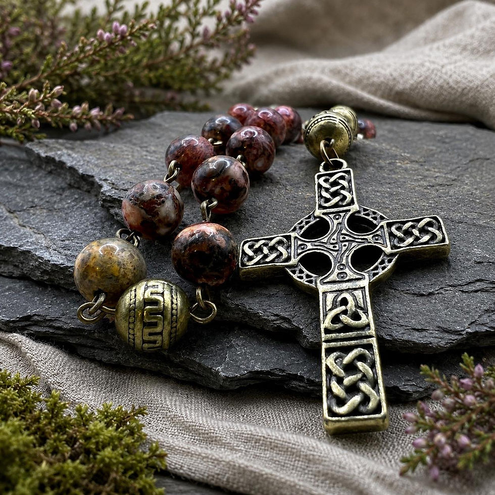 Pink granite Anglican prayer beads with antiqued brass Celtic cross on slate beside linen and heather.