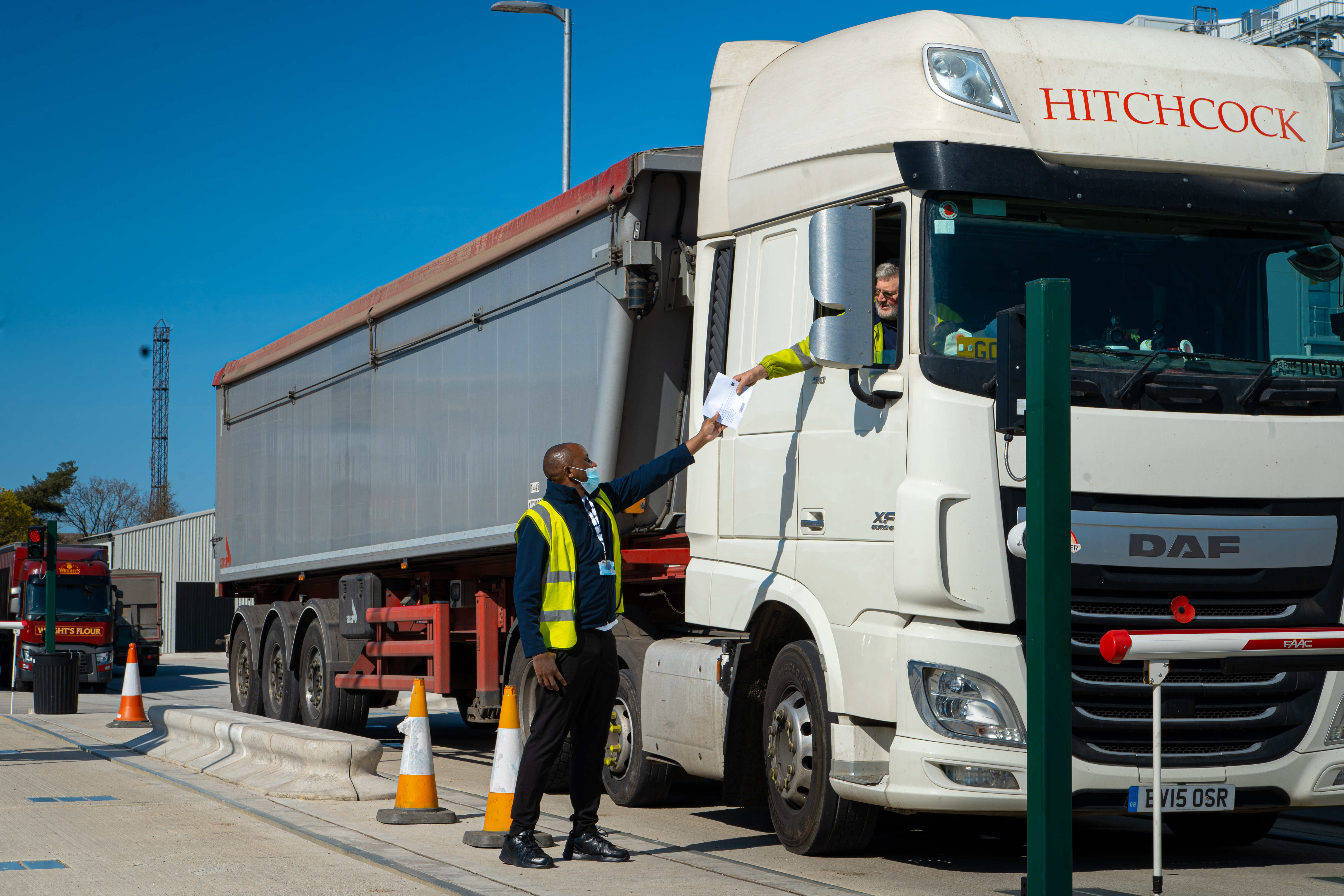 Security colleague exchanging delivery paperwork with an HGV driver at a site entrance
