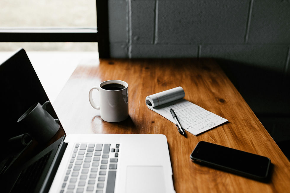 A desk with a laptop, notebook and cup of coffee.