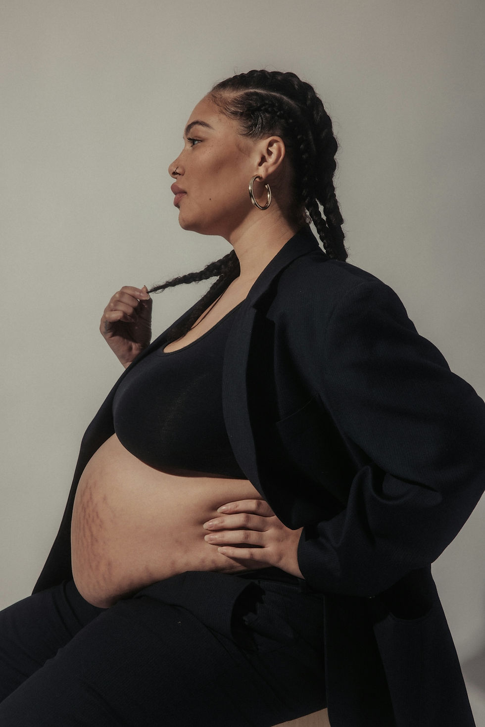 Black woman in a blazer with exposed pregnant belly and visible stretch marks, representing maternal strength and advocacy in Atlanta.