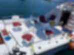 White boat deck with chairs and red cushions against blue water.